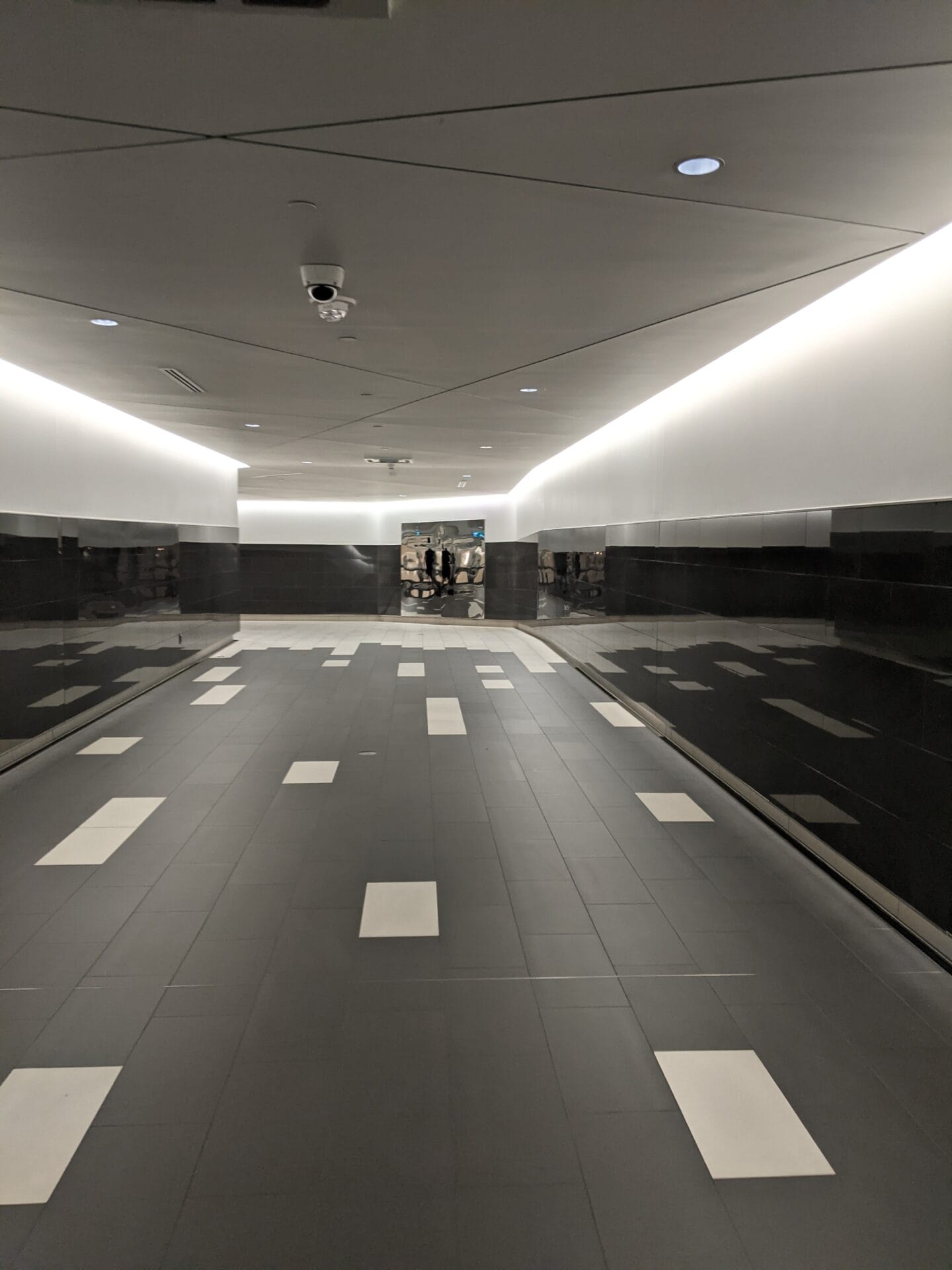 Tiled corridor with reflective walls and doorway at end of corridor