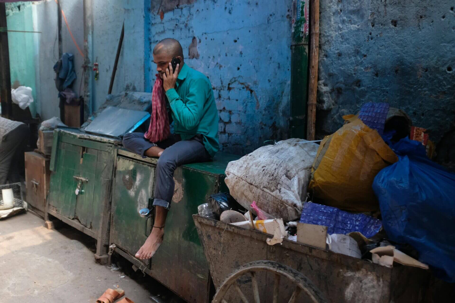 Man Sitting and Talking on Cellphone Near Garbage Dump. New Delhi, India