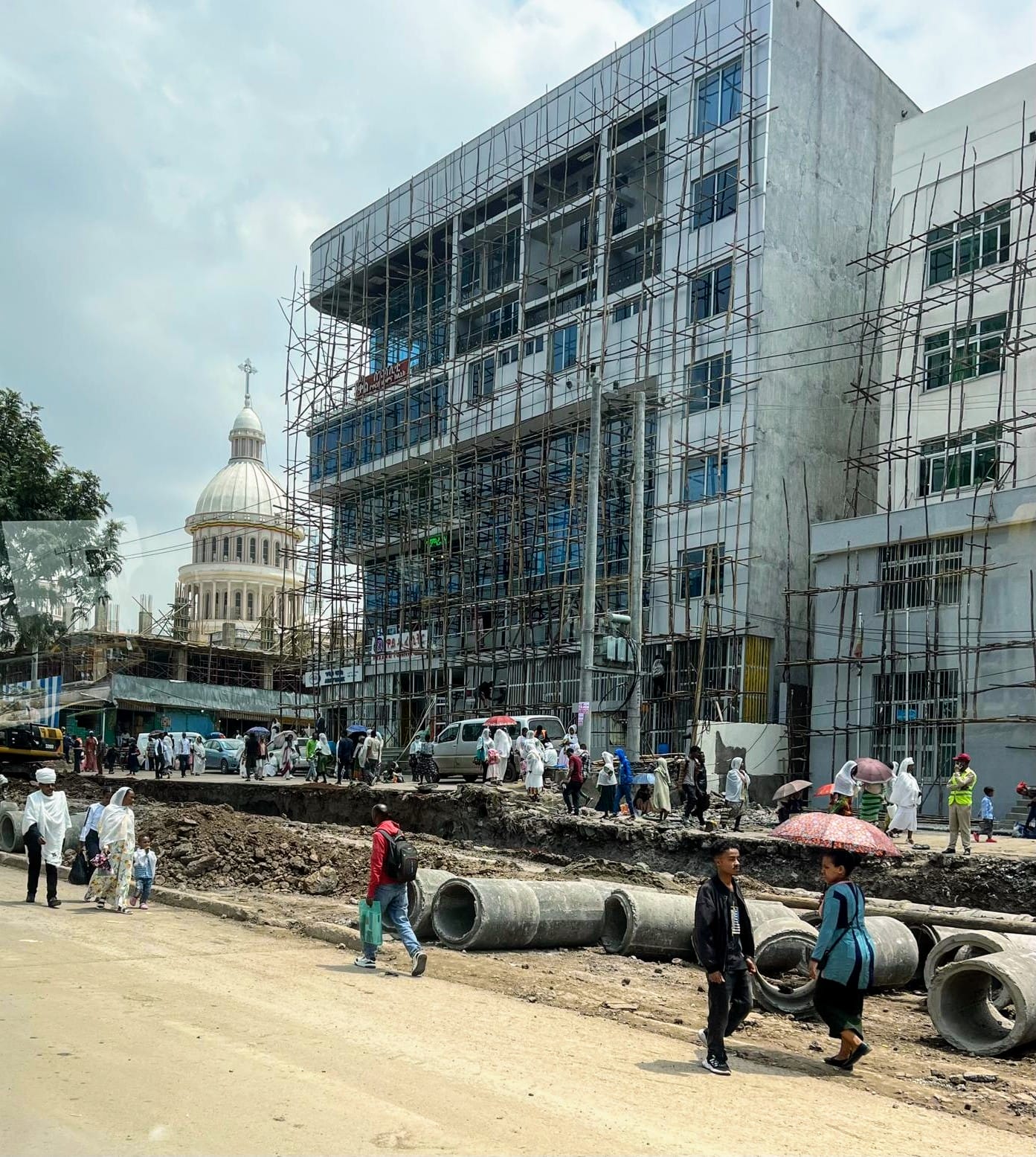 Pedestrians walk by scaffolding on buildings next to road construction
